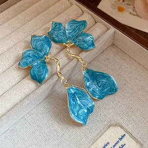 Detailed view of blue marbled enamel flower drop earrings in a textured jewelry box