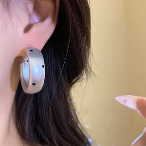 Detail view of matte silver oval hoop earrings with chic black polka dot pattern on ear