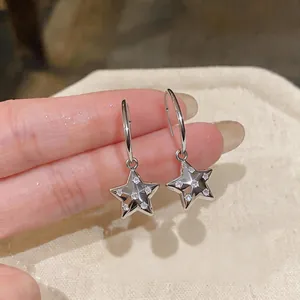 Dettaglio ravvicinato di orecchini a stella in zircone argento su fondo in tessuto.