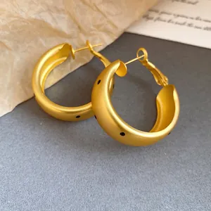 Close-up of elegant matte gold oval hoop earrings with stylish black polka dot accents.