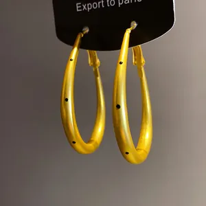 Detail view of gold-tone oval hoop earrings featuring black polka dot pattern design