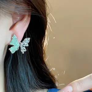 Détail d'une boucle d'oreille papillon en zircon et verre vert portée par un mannequin