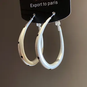 Detailed view of silver oval hoop earrings with black polka dots on a hanging card