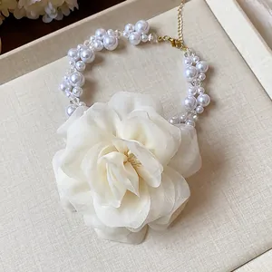 Close-up of white chiffon flower necklace with pearl and glass beads on a beige tray