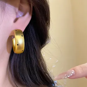 Detailed shot of wide matte gold hoop earrings with black polka dots worn on ear.