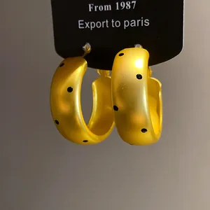 Macro detail of matte gold C-shaped hoop earrings with stylish black polka dot pattern.