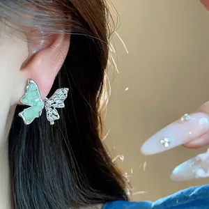 Gros plan d'une boucle d'oreille papillon scintillante avec verre vert et zircons sur l'oreille