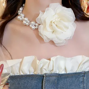 Close-up detail of an elegant pearl necklace featuring a large white layered chiffon flower.