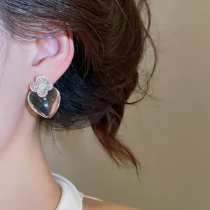 Gros plan de boucles d'oreilles transparentes en forme de cœur avec trèfle sur l'oreille.