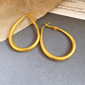 Close-up of matte gold oval hoop earrings with black polka dots and silver needles