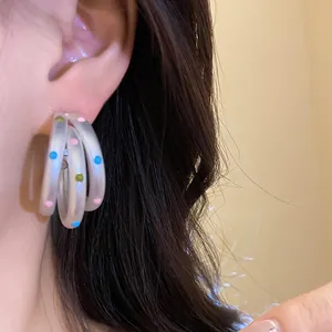 Close-up detail of matte oval multi-layer hoop earrings with colorful polka dots worn on ear