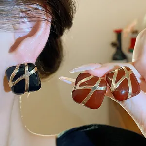 Close-up of retro square enamel earrings shown worn on ear and held in hand.
