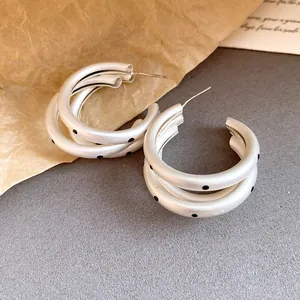 Close-up of elegant matte silver triple hoop earrings featuring black polka dot patterns.