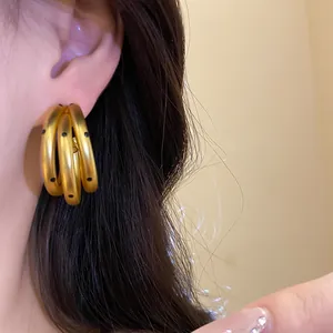 Close-up of matte gold triple hoop earrings with black polka dot details worn on ear.