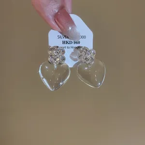 Détail de boucles d'oreilles cœur transparentes avec fleurs en cristal étincelantes