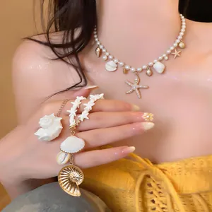 Close-up detail of a pearl necklace featuring shell and starfish charms worn by a model.