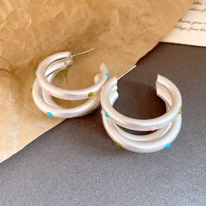Close-up of matte silver oval hoop earrings featuring vibrant colored polka dot enamel