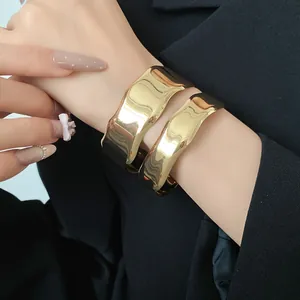 Close-up view of a wide irregular gold metal cuff bangle worn on wrist with glossy finish
