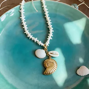 Close-up of ocean-themed necklace with shell and gold nautilus pendants on teal plate