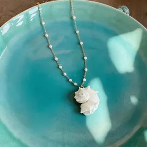 Detail of a conch shell pendant necklace with pearls on a teal ceramic plate.
