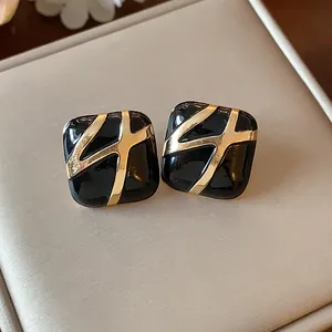 Close-up of vintage black enamel square stud earrings with gold cross design