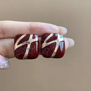 Close-up detail of vintage square red enamel stud earrings featuring gold abstract patterns