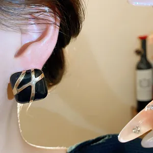 Close-up of retro black enamel square stud earrings with gold cross design on ear