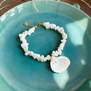 Detailed close-up of a white beach shell and pearl necklace displayed on a teal ceramic plate
