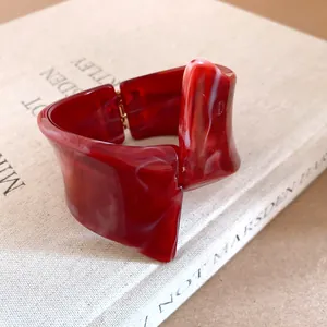 Detailed close-up of a red marbled resin bracelet with an irregular geometric twisted design.