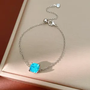 Elegant silver bracelet with square blue zircon detail on a textured beige jewelry display box.