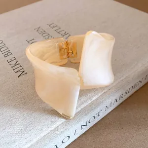Close-up of cream resin bangle with marbled texture and gold hinged clasp on a book