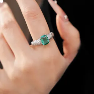 Exquisite emerald-cut green stone ring with silver-tone quilted pave band on finger