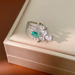 Close-up of a silver ring with emerald-cut green stone and pear-shaped zircons