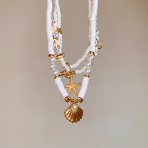 Detailed view of white clay and pearl beaded necklace with gold starfish and shell.