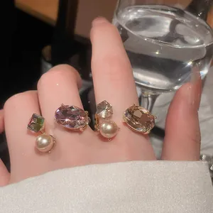 Close-up of luxury rhinestone and pearl open rings worn on a hand near a glass.