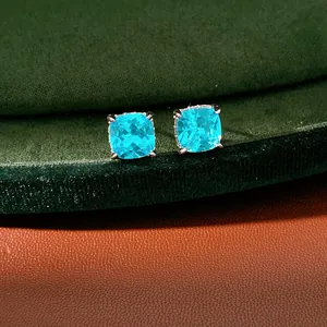 Close-up of square blue zircon stud earrings with silver prongs on green velvet display