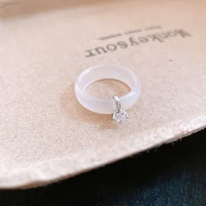Anillo redondo minimalista de calcedonia blanca con dije de circón sobre bandeja beige.