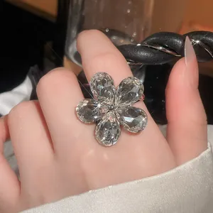 Close-up detail of a sparkling five-petal flower ring featuring pear-cut crystals on finger