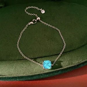 Detailed view of a silver necklace with a square light blue zircon on a green velvet base.