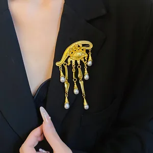 Dettaglio di una spilla vintage a forma di occhio dorato con nappe di perle sul blazer.