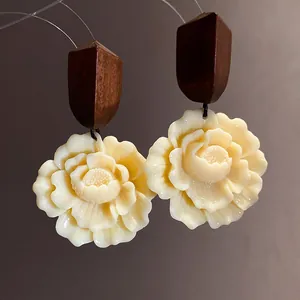 Detailansicht von eleganten Ohrringen mit dunklem Holz und cremefarbenem Blütenanhänger.