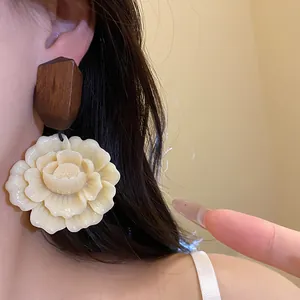 Nahaufnahme eleganter Blumenohrringe aus Kunstharz mit dunklem Holzstecker am Ohr