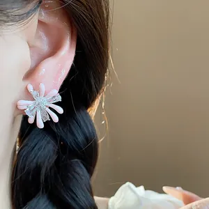 Close-up of delicate pink flower zircon stud earrings with silver needles on ear