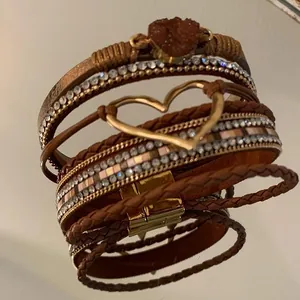 Close-up of bohemian multi-layer leather bracelet with gold heart and rhinestone bands