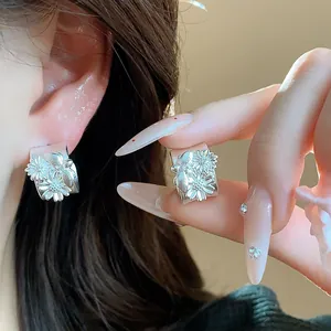 Primer plano de pendientes de tuerca en forma de C de plata mate con diseño de flores