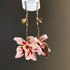 Close-up of elegant pink enamel flower drop earrings with a stylish golden branch design