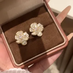 Detailed view of elegant white camellia stud earrings with crystals in a jewelry box