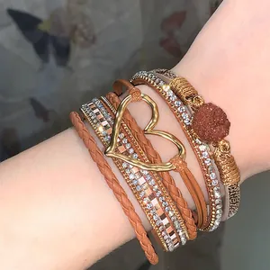 Close-up of bohemian multi-layer leather bracelet with golden heart and rhinestones.