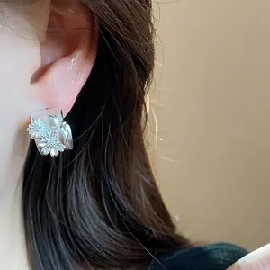 Primer plano de pendientes de botón en C plateados mate con delicado diseño de flores