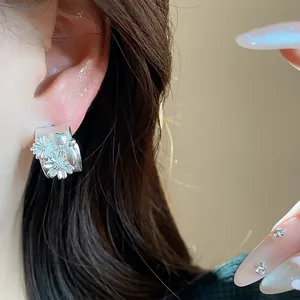 Vista detallada de pendientes de flores en forma de C de plata mate con circonitas en modelo.